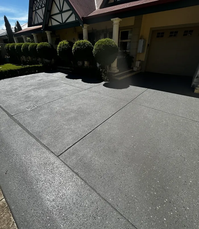 Dark grey resurfaced concrete driveway in front of a Tudor-style home with a garage