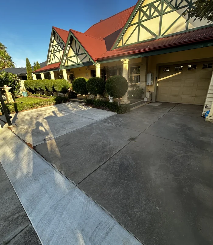 Worn concrete driveway in front of a Tudor-style home with a garage, before resurfacing