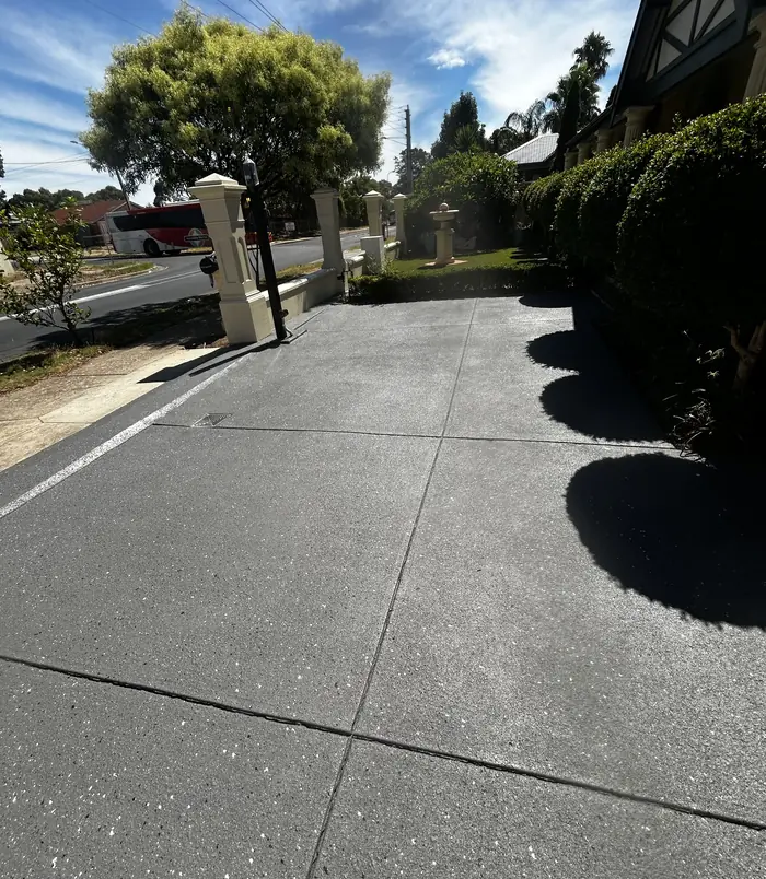 Dark grey resurfaced concrete driveway beside a hedge and front gate pillar