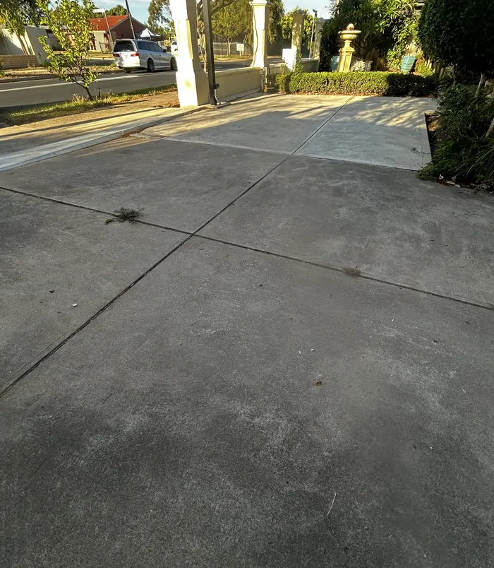 Pale, cracked concrete driveway in front of a garage, before concrete resurfacing