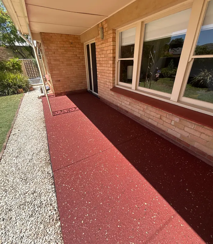 Rich red resurfaced concrete patio beside a brick home