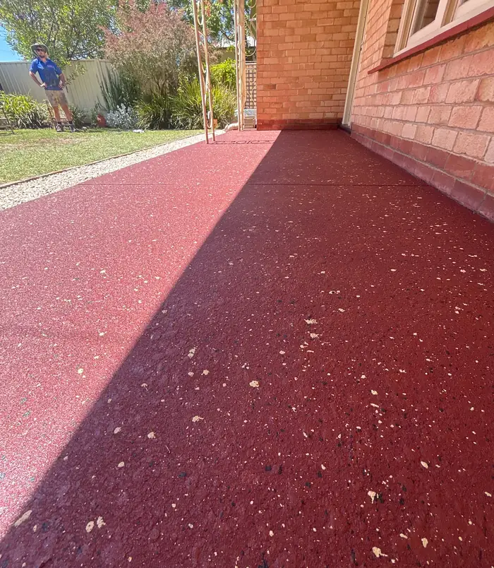 Deep red resurfaced concrete path with a speckled finish beside a brick wall and lawn