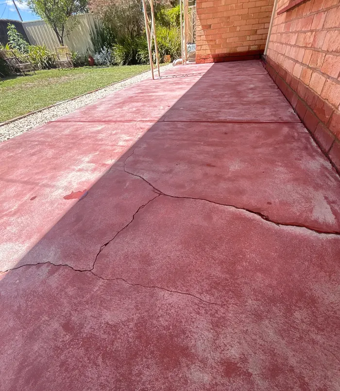 Cracked, faded pink concrete path beside a brick wall and lawn, before concrete resurfacing