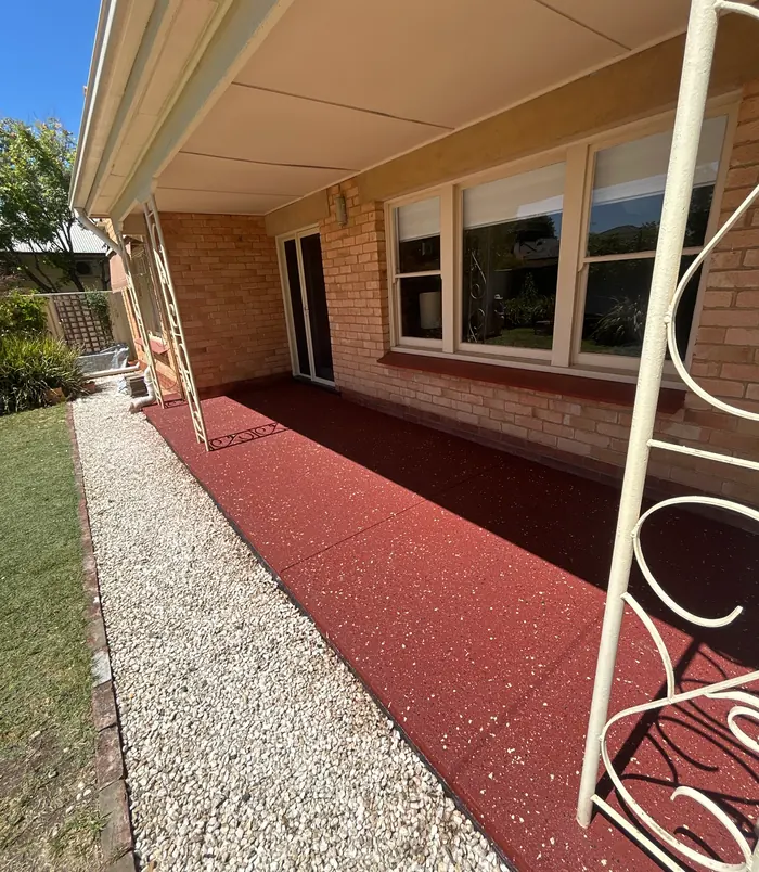Rich red resurfaced concrete patio beside a brick home with large windows