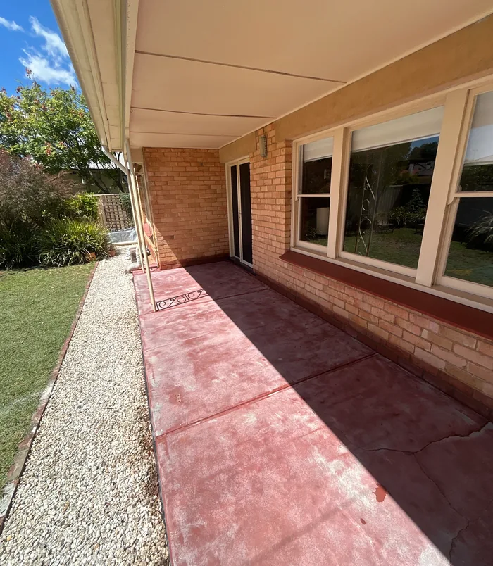 Faded red concrete patio beside a brick home with large windows, before concrete resurfacing