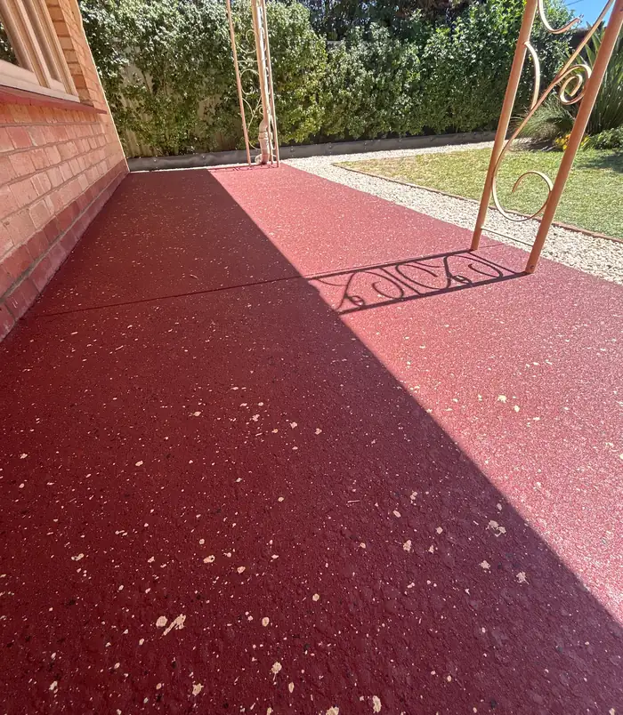 Deep red resurfaced concrete patio with a speckled finish beside a brick wall