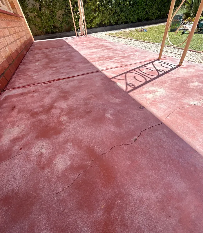 Faded, blotchy pink concrete patio beside a brick wall and veranda post, before resurfacing