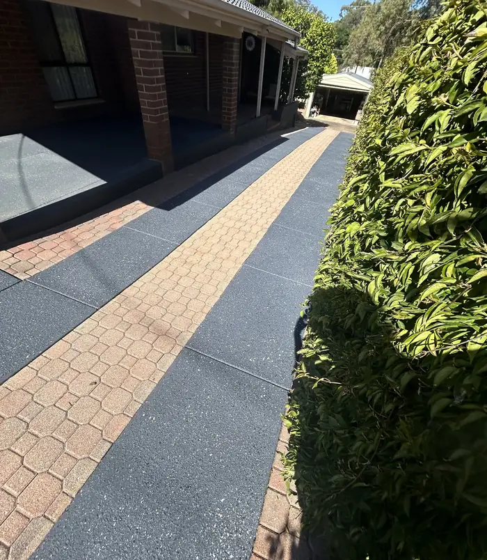 Dark grey resurfaced concrete path with a brick paver strip beside a hedge