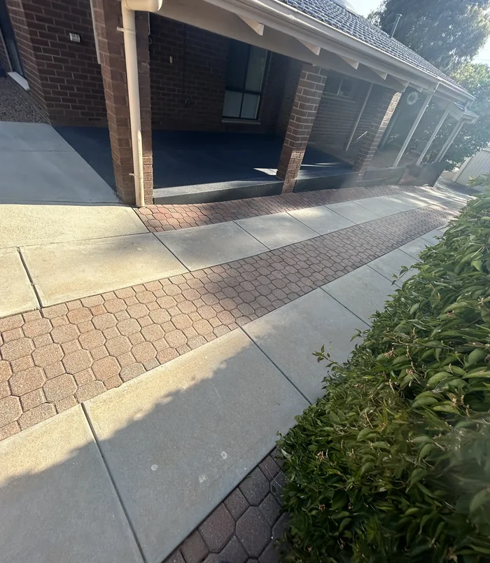 Pale concrete path with a brick paver strip beside a carport, before concrete resurfacing