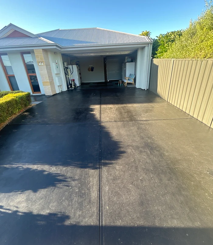 Stained, patchy concrete driveway in front of a carport and cream home, before resurfacing