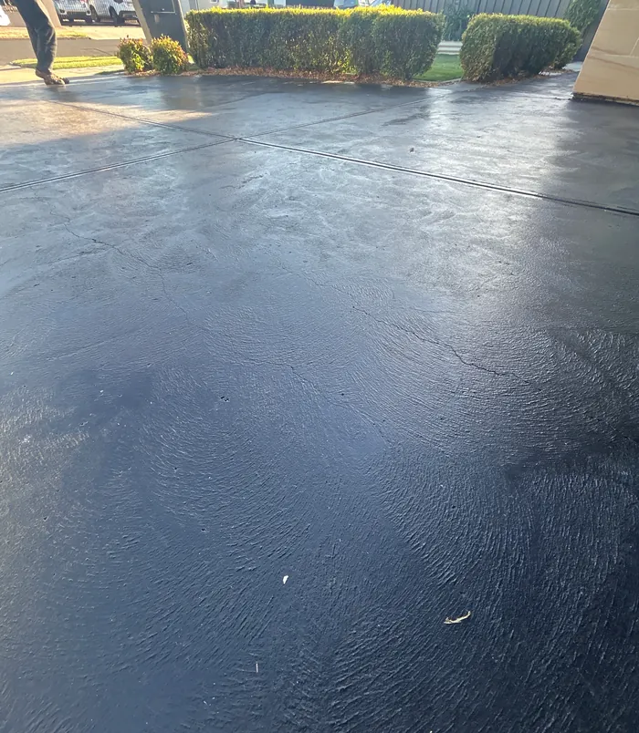 Glossy, uneven dark concrete surface with a patchy finish, before concrete resurfacing