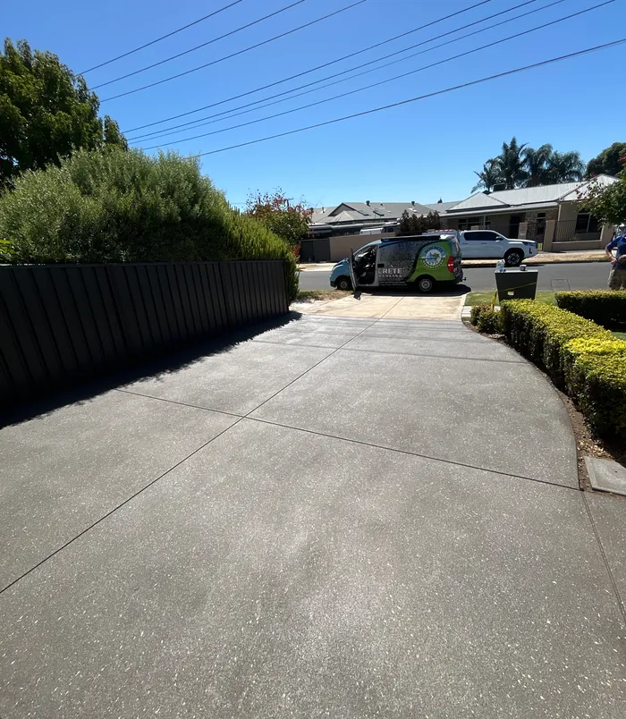 Dark grey resurfaced concrete driveway beside a fence and hedge