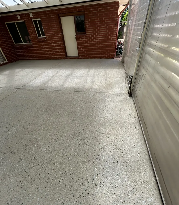 Clean grey resurfaced concrete beside a red brick wall and roller shutter