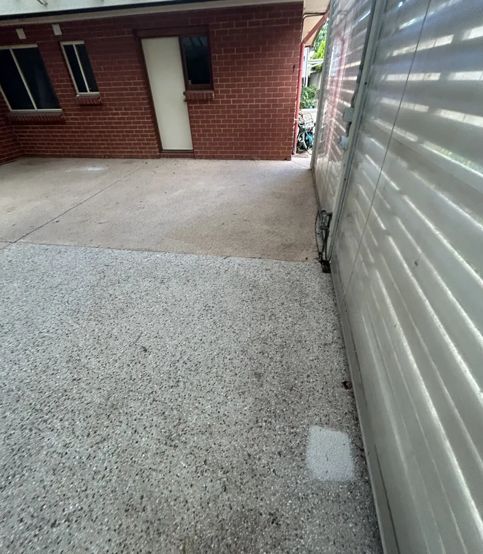 Stained beige concrete beside a red brick wall and roller shutter, before concrete resurfacing