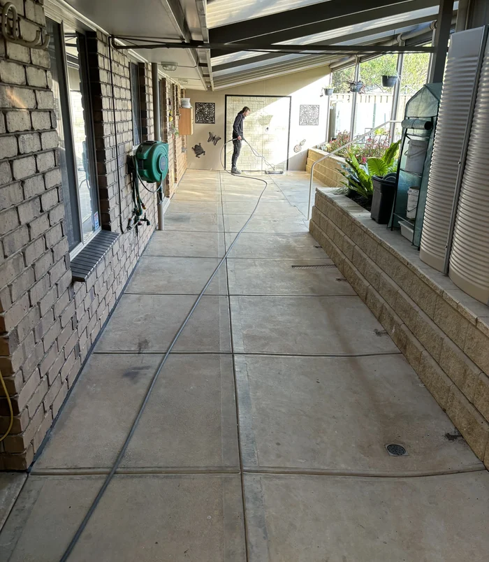 Pale, worn concrete walkway beside a brick wall and covered veranda, before concrete resurfacing