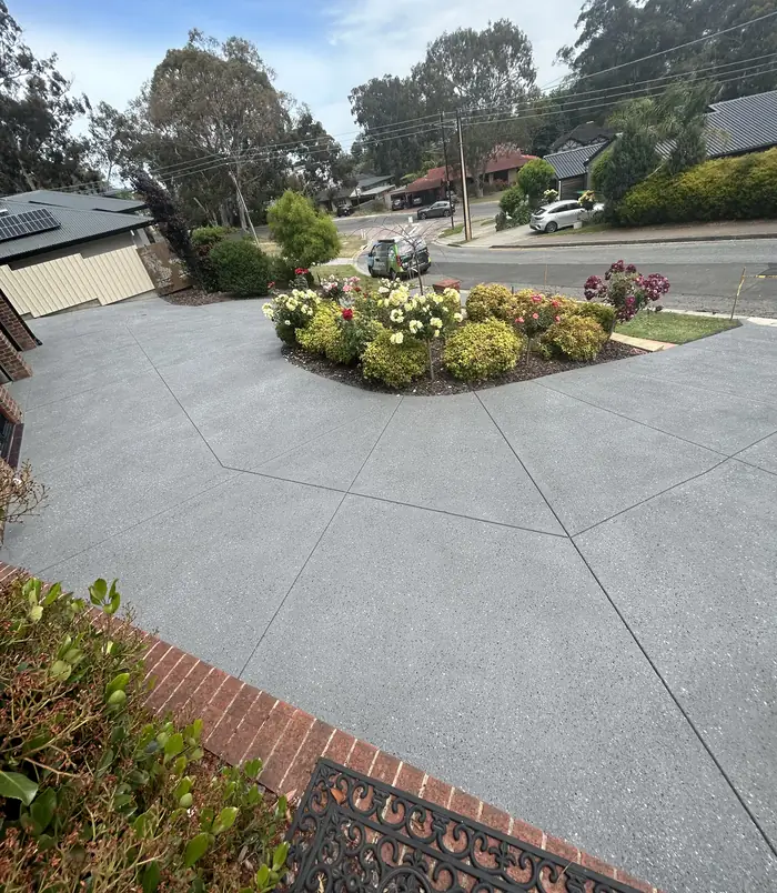 Clean light grey resurfaced concrete driveway curving around a flowering garden bed