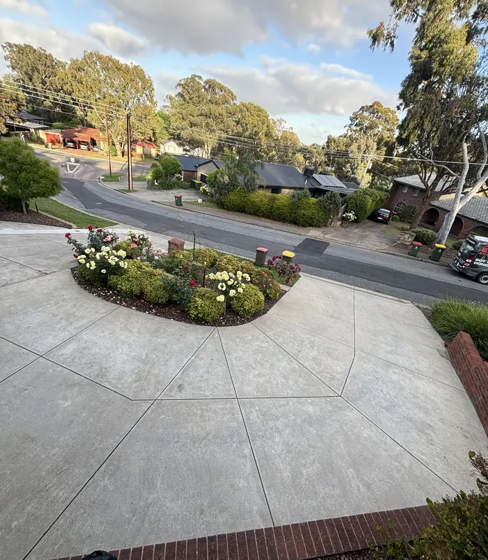 Worn concrete driveway curving around a flowering garden bed beside a street, before resurfacing