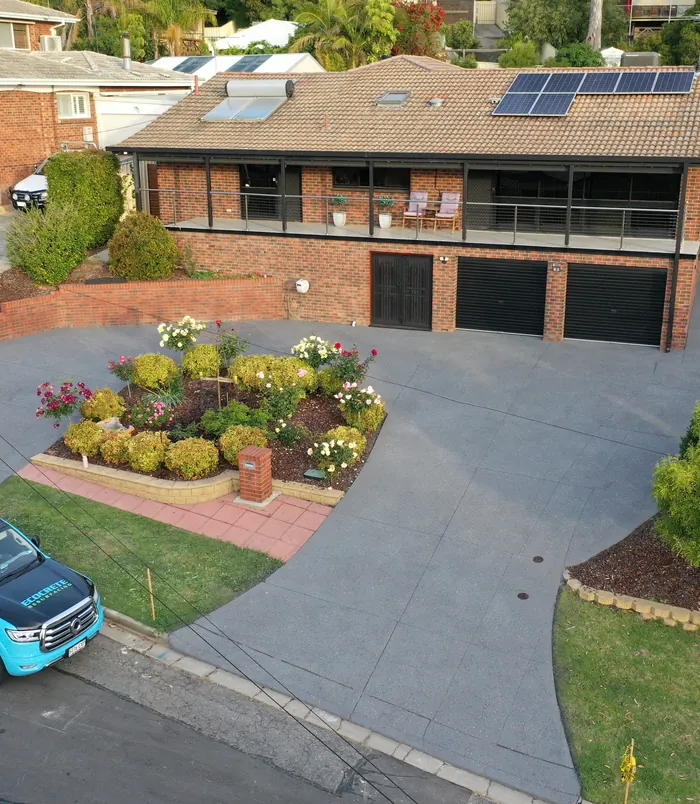Clean light grey resurfaced concrete driveway curving around a flowering garden bed