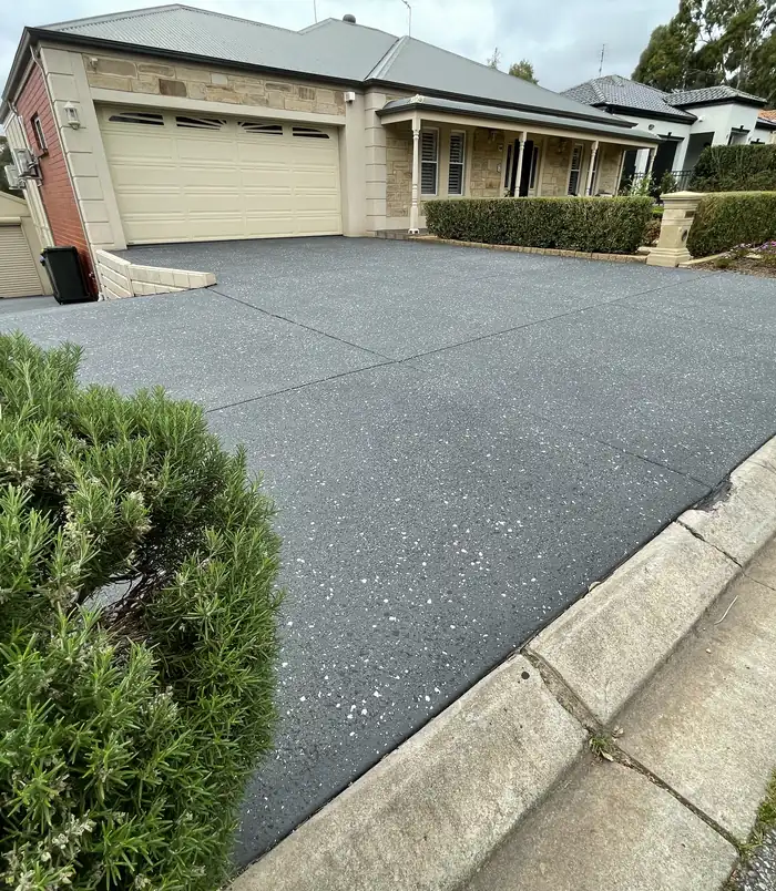 Dark grey resurfaced concrete driveway around a flower garden in front of a two-storey home