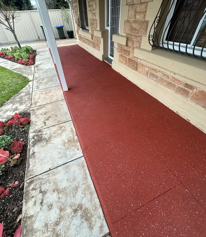 Bright red resurfaced concrete path beside a sandstone home and garden