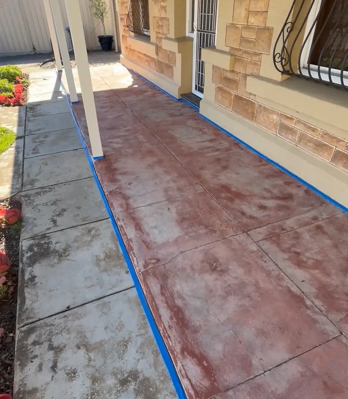 Faded, stained red concrete path beside a sandstone home with blue masking tape, before resurfacing