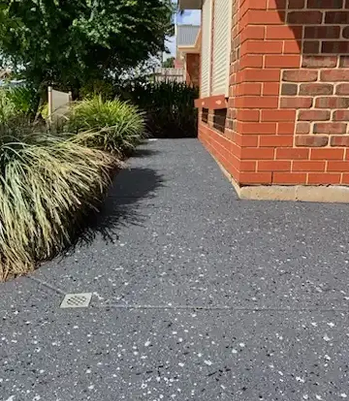 Dark grey resurfaced concrete path beside a red brick wall and garden grasses