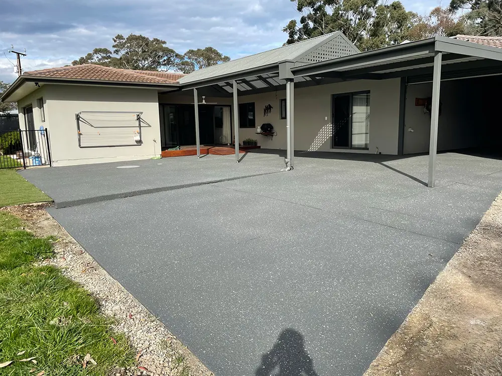 Grey concrete area in front of a single-storey home with a carport