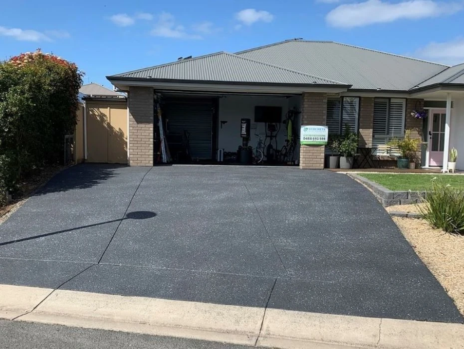 Freshly sealed dark driveway leading to a brick home with a double garage