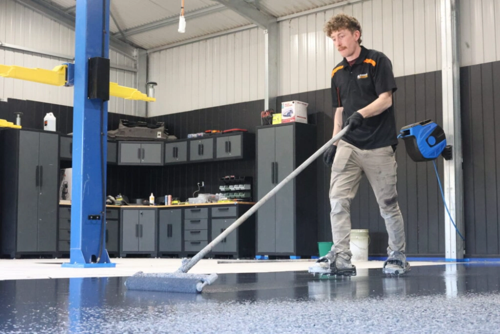 Surface Rescue team member rolling coating onto a garage floor beside a car hoist