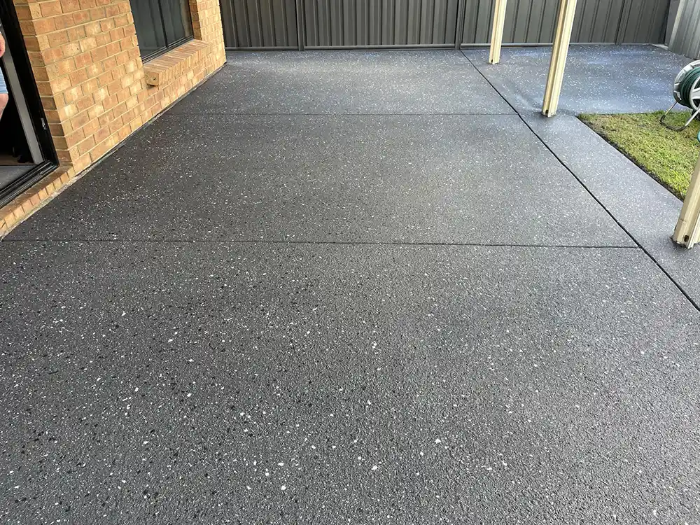 Dark speckled sealed concrete patio beside a brick wall