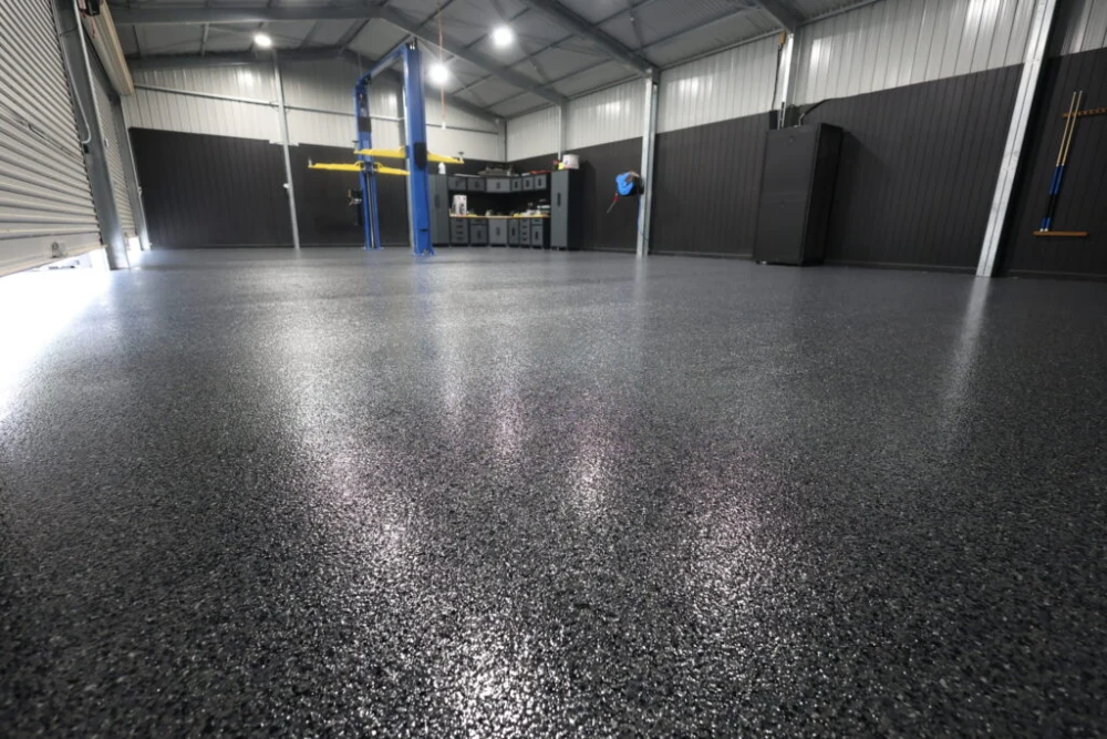 Garage with a dark speckled epoxy flake floor and a vehicle hoist