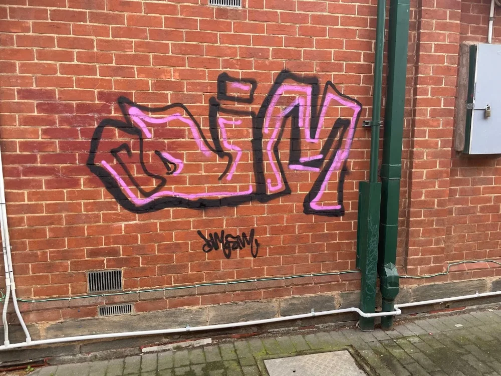 Pink and black graffiti tag on a red brick wall beside a green downpipe