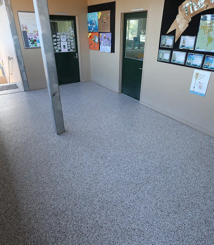 Grey speckled epoxy flake floor in a school corridor with notice boards and a green door