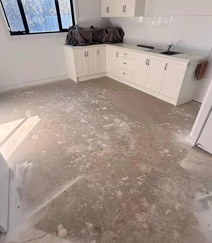 Dirty, uneven concrete floor in a commercial kitchenette with white cabinetry, before epoxy flooring