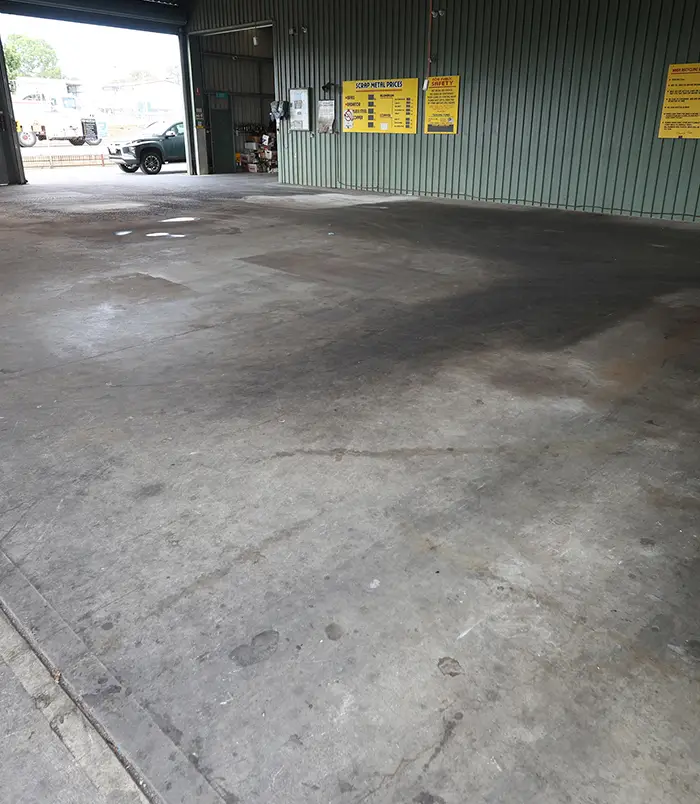 Stained, dusty concrete floor in an industrial building with yellow signs, before epoxy flooring