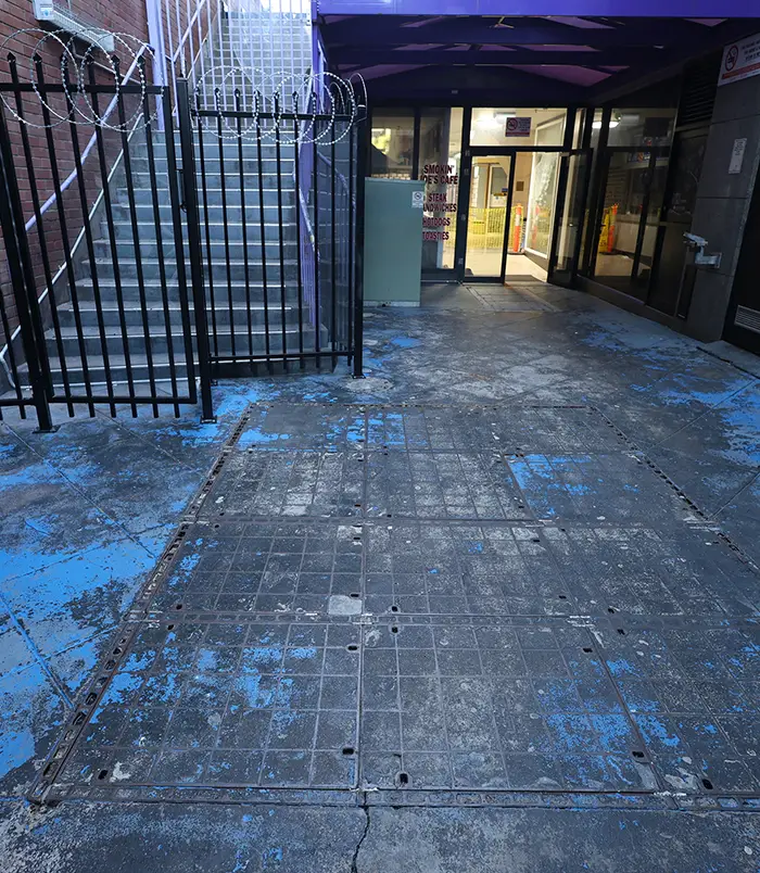 Stained, dusty concrete entry floor beside a black gate and staircase, before epoxy flooring