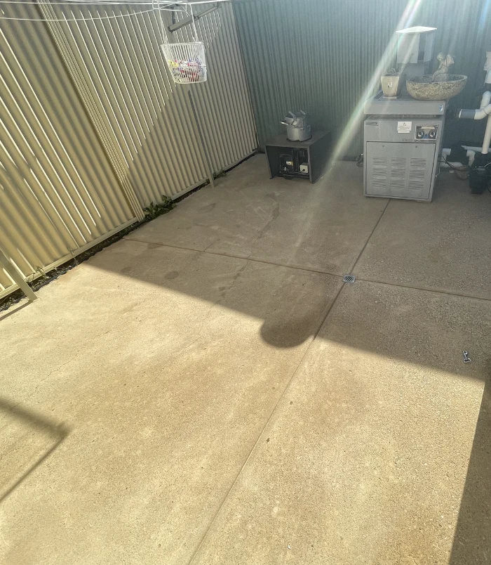 Clean concrete courtyard beside a fence with a pool pump and equipment