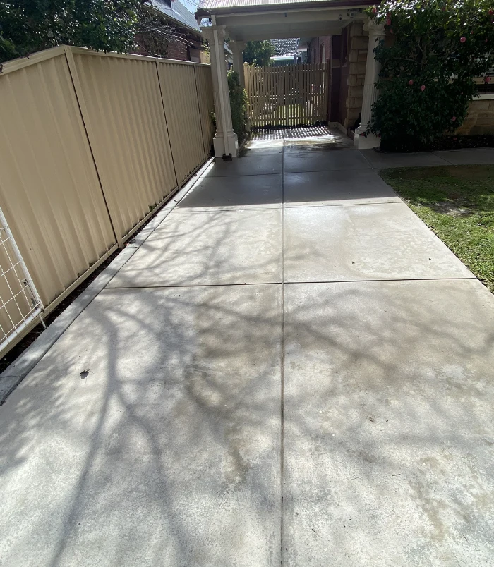 Clean, light concrete driveway beside a tan fence and carport