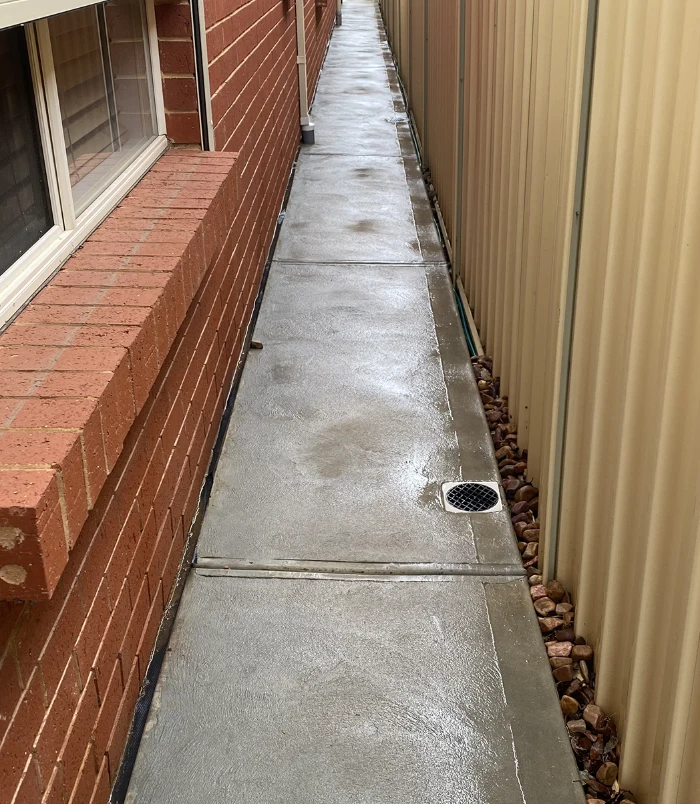 Clean concrete side path between a brick wall and a tan fence