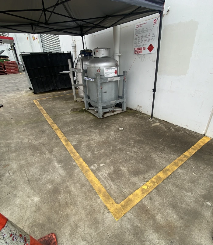 Stained commercial concrete floor around a stainless steel tank with yellow line markings, before concrete cleaning