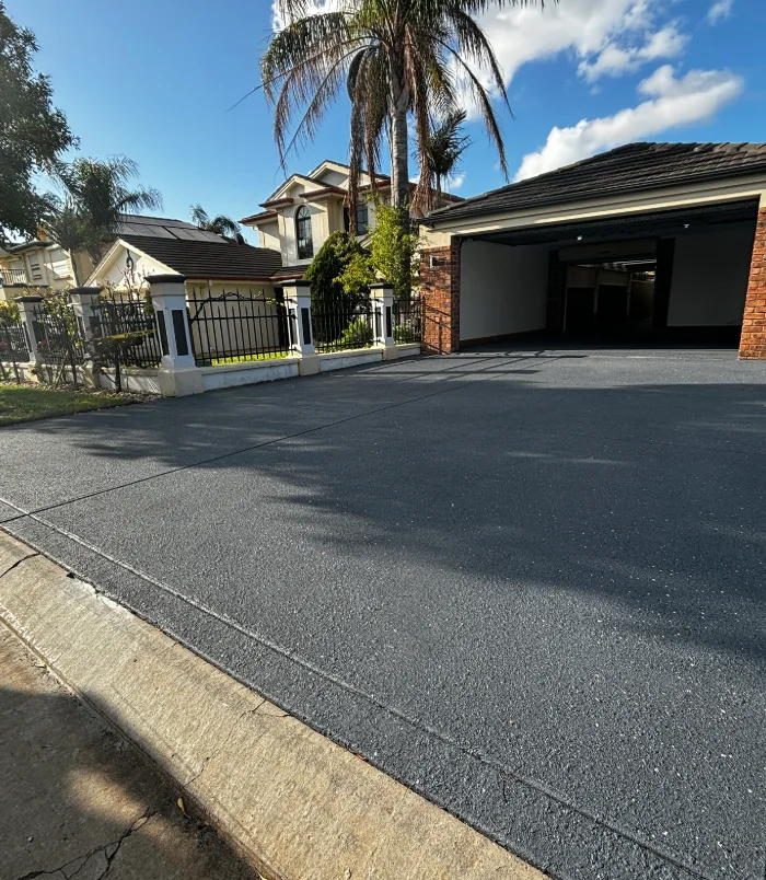 Dark grey resurfaced concrete driveway in front of a double garage and palm trees