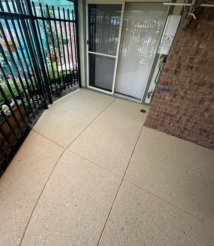 Clean, light resurfaced concrete entry beside a black fence and glass door