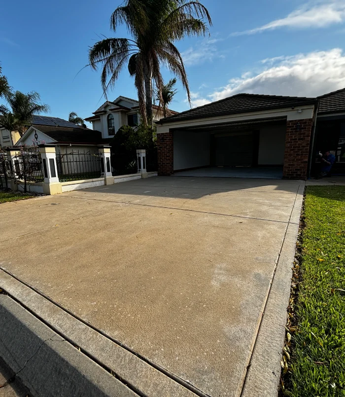 Pale, weathered concrete driveway in front of a double garage and palm trees, before concrete resurfacing