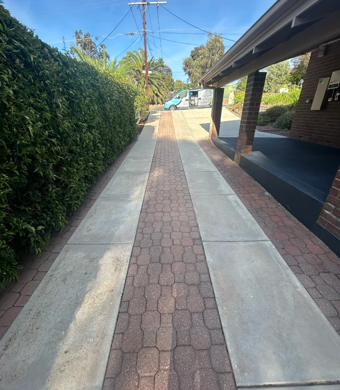 Pale, worn concrete driveway leading to a double garage beside a hedge, before resurfacing