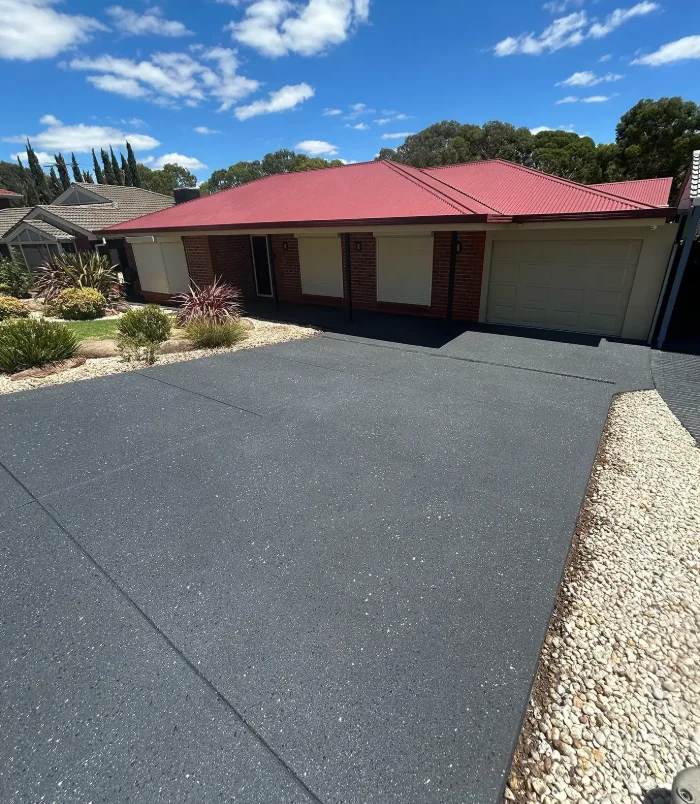 Dark grey resurfaced concrete driveway in front of a home with a cream garage door and hedge