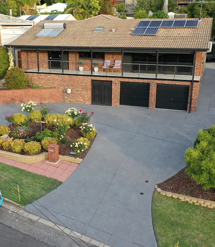 Dark grey resurfaced concrete driveway around a flower garden in front of a two-storey home