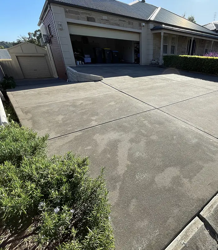 Faded, patchy pink concrete driveway in front of a brick home with a red roof, before resurfacing