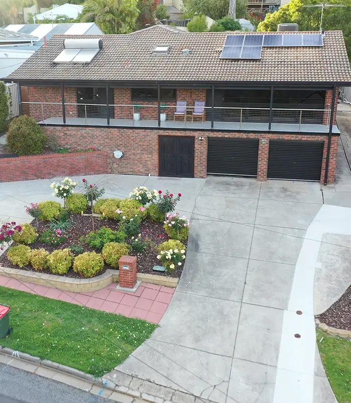 Pale concrete driveway around a garden bed in front of a two-storey home, before resurfacing