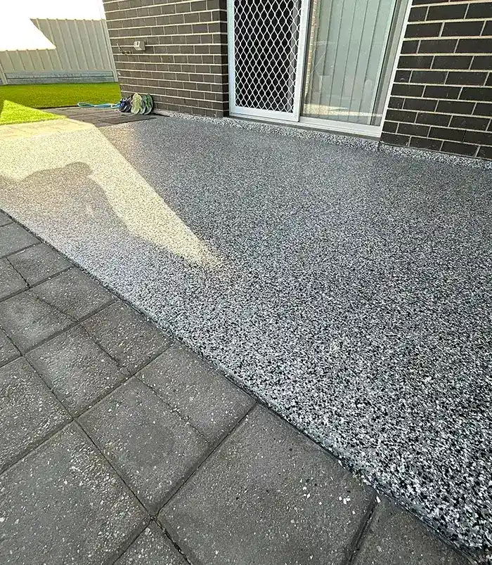 Grey speckled epoxy flake patio floor beside a dark brick wall and sliding door
