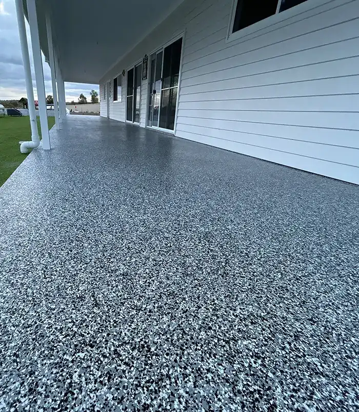 Blue-grey speckled epoxy flake veranda floor beside a white weatherboard house and lawn